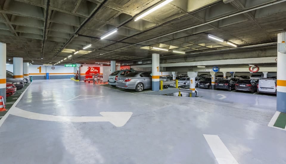 Parking subterráneo a pie en Barcelona, ​​ideal para aparcar barato. Vista de un estacionamiento moderno con varios autos estacionados, bajo un techo de concreto, cerca de un centro comercial o edificio.