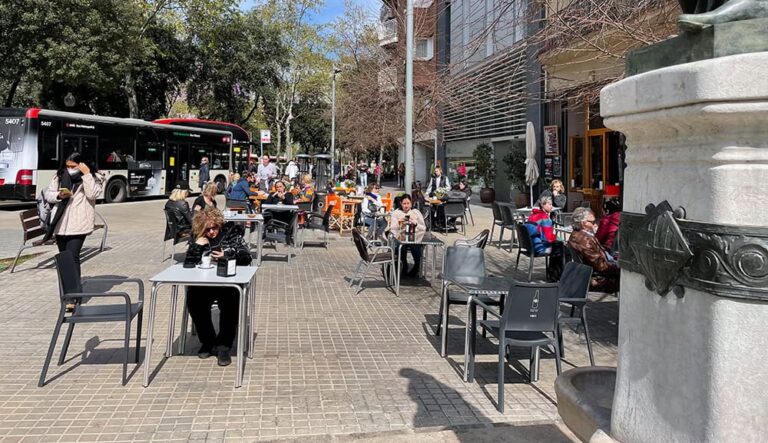 Concurrida terraza de cafetería con clientes disfrutando del sol al aire libre.