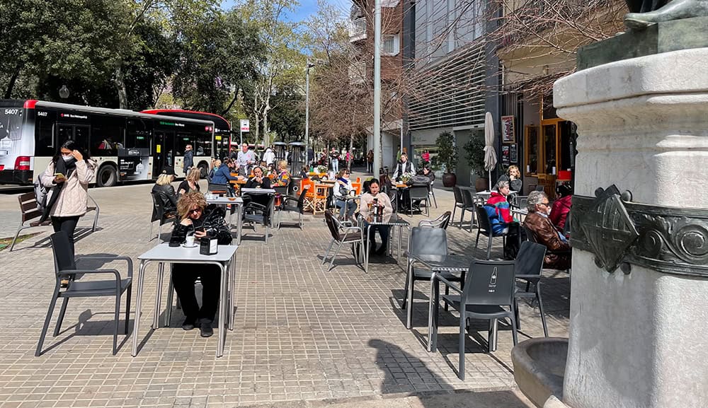 Concurrida terraza de cafetería con clientes disfrutando del sol al aire libre.